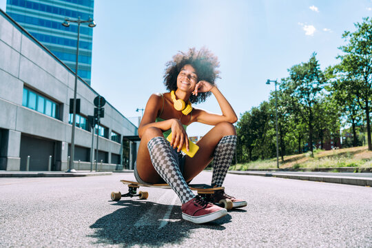 Smiling young woman with smart phone sitting on skateboard