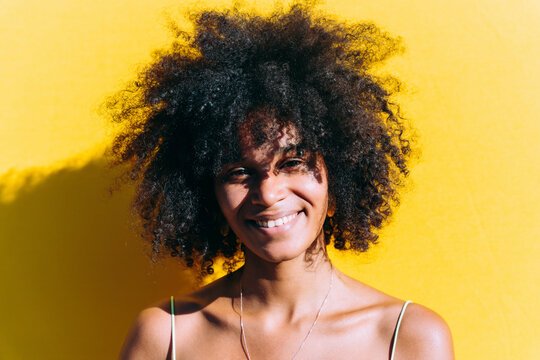 Happy Woman With Afro Hairstyle In Front Of Yellow Wall