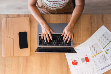 Businesswoman typing on laptop keyboard by document at desk in office