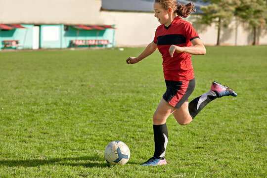 Girl kicking soccer ball at field on sunny day