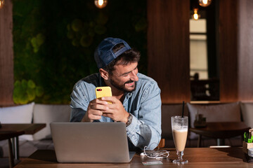 Young man working remote from caffe bar, using phone and laptop.
Buying online