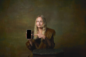 Portrait of young girl as Mona Lisa picture pointing at device screen over dark vintage background. Retro style, art, fashion, comparison of eras concept.