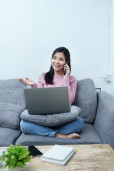 Portrait of a beautiful Asian teenage girl using her phone and computer sitting on the sofa at home