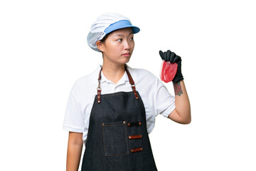 Young caucasian woman wearing an apron and serving fresh cut meat over isolated background looking to the side