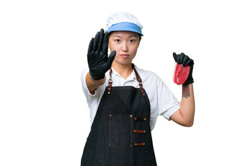 Young caucasian woman wearing an apron and serving fresh cut meat over isolated background making stop gesture