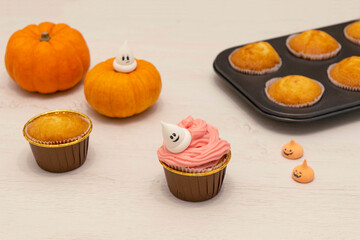 Caucasain woman decorating freshly made cupcakes or maffins with cream at the kitchen