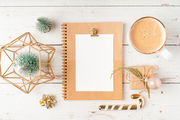 Top view Desktop Christmas notepad with mockup blank paper. Flat lay on white wooden table background with planner, coffee cup, tree brunch, Christmas eco nature decoration, notebook and stationery.