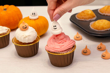 Caucasain woman decorating freshly made cupcakes or maffins with cream at the kitchen