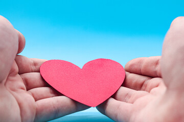 Obraz premium hands holding a red paper heart on a blue background. health care, hope, life insurance concept, world heart day, world health day, organ donor day, csr social responsibility, gratitude