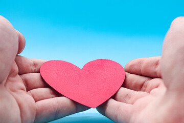 hands holding a red paper heart on a blue background.
 health care, hope, life insurance concept, world heart day, world health day, organ donor day, csr social responsibility, gratitude