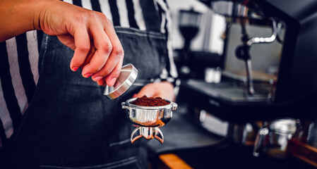 Barista holding portafilter and coffee tamper making an espresso coffee in cafe