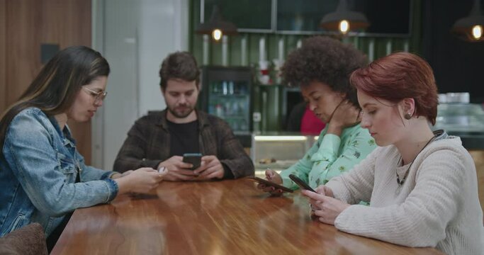 Group of diverse people in front of their modern devices at coffee shop isolated together. Friends each in technological bubbles staring at smartphone screens