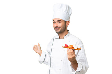 Young caucasian chef holding a sushi over isolated background extending hands to the side for inviting to come