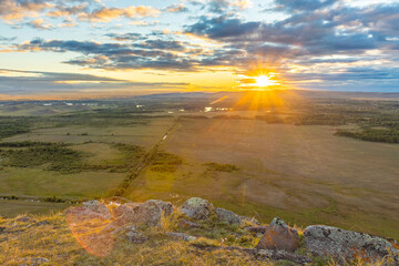 Golden sunset over the autumn Khakas steppe. Top view from the mountain range to the valley. The bright sun shines through the clouds of the evening sky