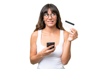 Young caucasian woman over isolated background buying with the mobile with a credit card while thinking