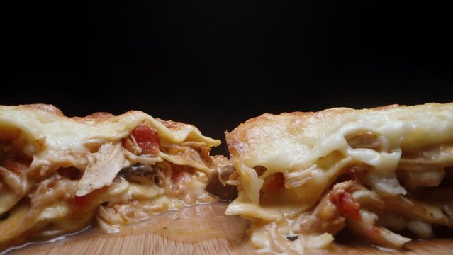 Two pieces of lasagna on a wooden table. Black background, close-up.