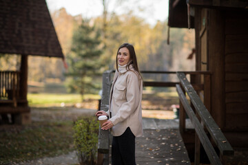 Young happy woman relaxing with hot tea or coffee on the cozy terrace of a wooden country house. Autumn cozy day.