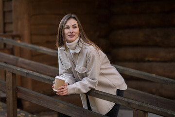 Young happy woman relaxing with hot tea or coffee on the cozy terrace of a wooden country house....