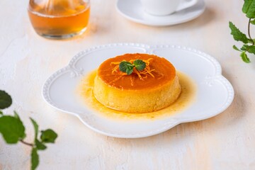 Pumpkin flan, a cold baked dessert of pumpkin puree, eggs, cream and sugar with caramel on a white plate on a light concrete background. Thanksgiving, Halloween