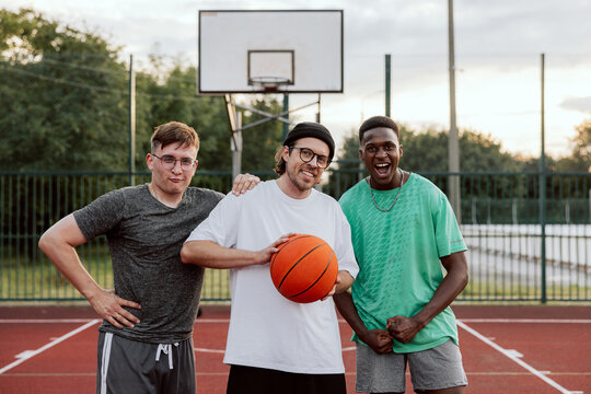 Portrait photo of delighted friendship company outside playing basketball in free time showing skills trying to make slam dunk. Fit sporty guys.
