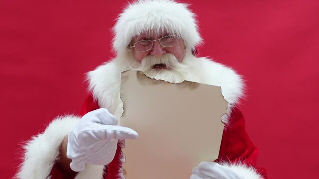 Real Santa Claus pointing on christmas letter, red studio background. Xmas time. 