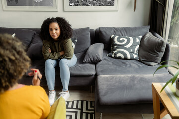 An African-American teen girl sits on a couch and talks to the unrecognizable female...