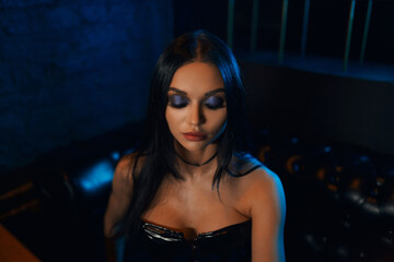 A sexy and beautiful woman enjoys a hookah in a nightclub. Glamorous clothes and neon lights.