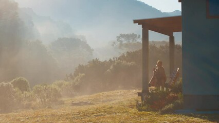 Woman drinks mate tea and enjoys sunrise in Brazilian mountains from the wooden terrace