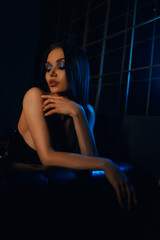 A sexy and beautiful woman enjoys a hookah in a nightclub. Glamorous clothes and neon lights.