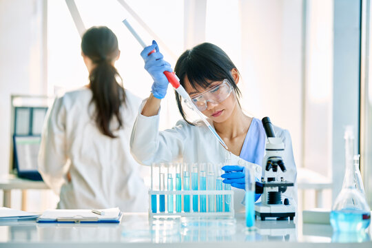 Female scientist making microbiology research using pipette, flask and test tubes working in modern chemical lab