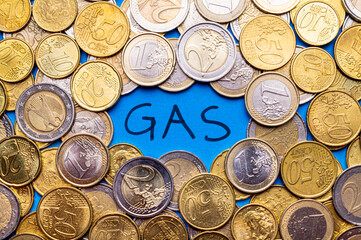 Text "gas" in black color, on a blue surface, and coins around it. Price hikes and gas hike speculations.