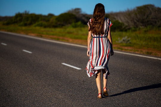 a beautiful long-haired girl in a long dress walks along a road in the desert in western australia, a beautiful girl lost in the middle of nowhere in the australian outback