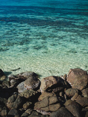 Scenic view of Sunset Beach, Koh Lipe Island. Rocky coastline against crystal clear turquoise sea with coral reef transparent shallow water. Satun, Thailand. Natural background with copy space.