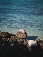 Scenic view of Sunset Beach, Koh Lipe Island. Crystal clear turquoise sea with coral reef transparent shallow water and rocky coastline foreground. Satun, Thailand. Minimal summer vibe.