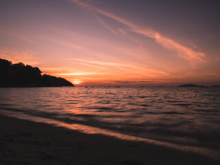 Scenic view of Sunset Beach, Koh Lipe Island. Dramatic sunset orange sky with sunlight reflection on sea water waves. Satun, Thailand. Long exposure, blurred wave motion.