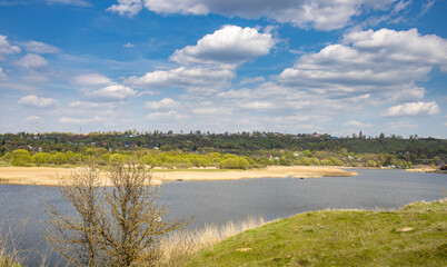 Sunlight through the clouds illuminates the young greenery of bushes and trees. Rural spring landscape with a river, clouds over the horizon.