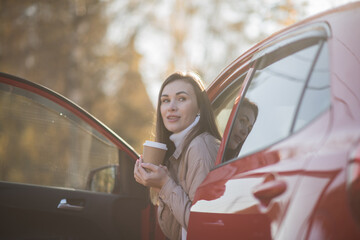 happy brunette girl travels in autumn in a red car and warms up with hot coffee, the concept of travel and autumn holidays, vacation