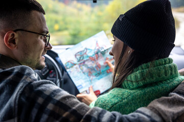 A man and lady holding and looking at paper map, sitting inside car.