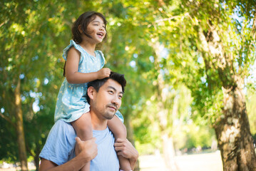 Happy Asian father with daughter on his neck. Happy man enjoying rest in park and little girl...