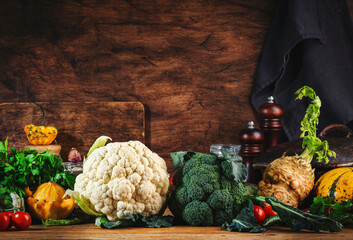 Autumn food background with organic farm vegetables: cauliflower, broccoli, root celery, pumpkin, herbs and spices on rustic wood kitchen table with cast iron pan, spice grinders, cutting board