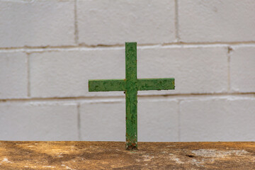 Uma cruz verde com uma parede branca de tijolos ao fundo. 