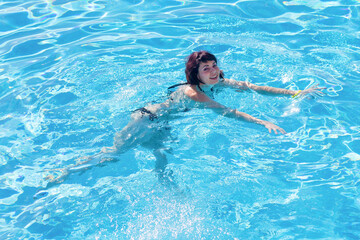 Fototapeta na wymiar Young brunette woman swims in the blue water of the pool.