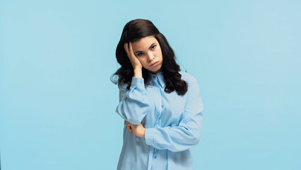 displeased young woman in shirt touching head while puffing cheeks isolated on blue