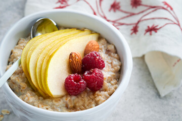 Oatmeal. Bowl of oatmeal porridge with raspberry, pear and honey on gray concrete old table background. Hot and healthy food for Breakfast, top view, flat lay