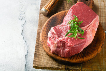 Raw beef steak. Fresh beef rib eye steak with fork rosemary, salt and pepper on piece of parchment paper on old wooden background. Top view. Mockup for design idea.