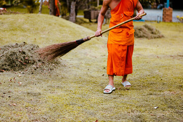 The monk sweeps leaves to collect trash in the temple courtyard.