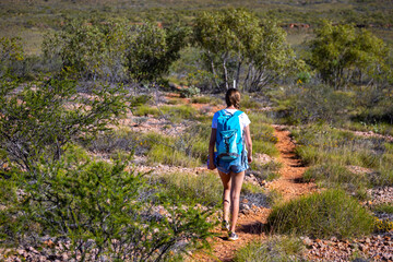 fit girl with backpack hiking uphill on red rocks in cape range national park in western australia,...