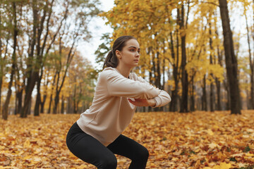 Focused fit sportswoman doing squat exercise while having fitness training in autumn park and leading healthy lifestyle 