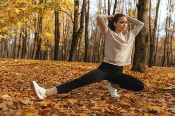 Sporty confident woman making ponytail while doing side lunge exercise and training in autumn park...