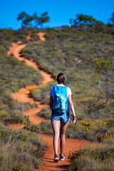 fit girl with backpack hiking uphill on red rocks in cape range national park in western australia,...